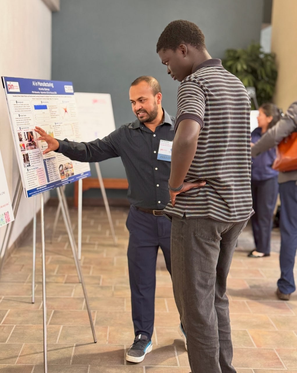 One person gestures toward a project poster while another listens.